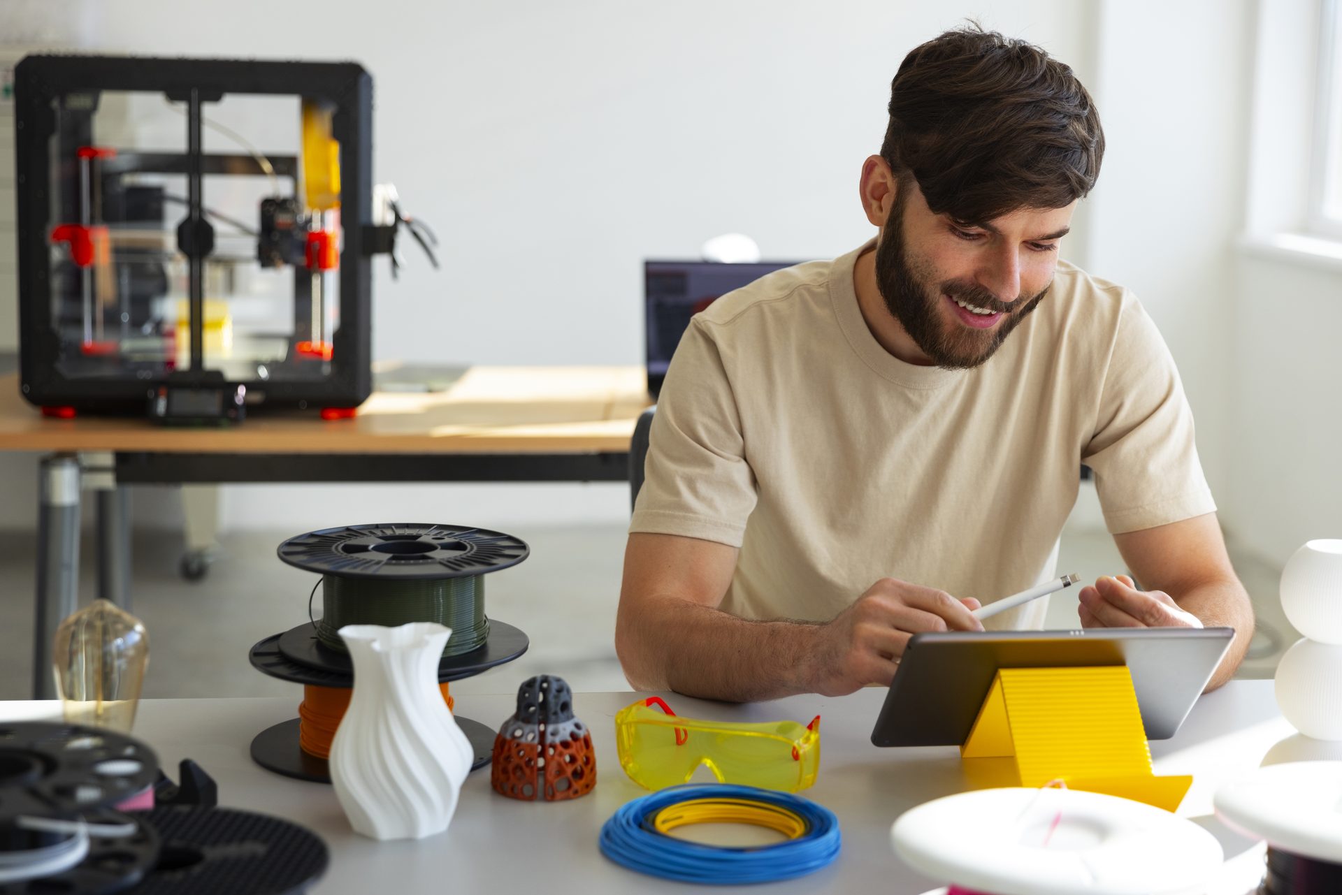 Joven diseñador trabajando con una impresora 3D y una tablet en un taller de prototipos